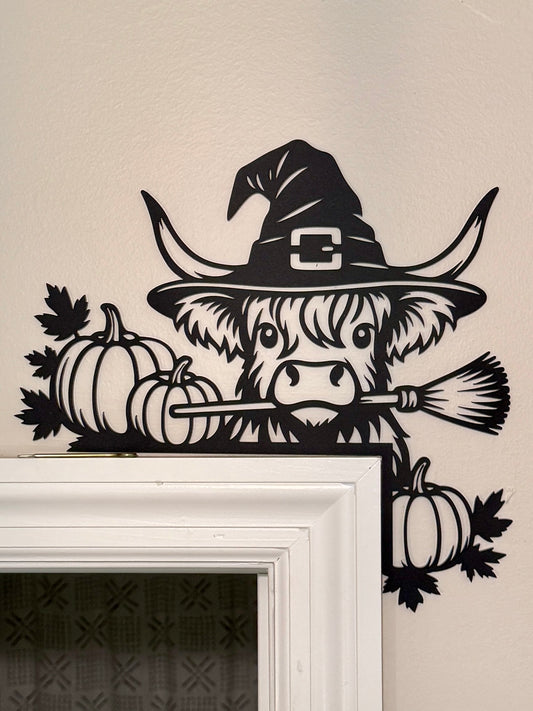 Decorative door decor of a cow wearing a witch hat with pumpkins and a broomstick.